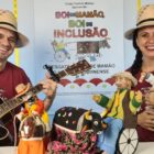 Um ator e um atriz com chapéus seguram instrumentos musicais sentados
