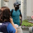 Três funcionários da Prefeitura uniformizados conversam com ambulante na rua