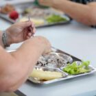 Duas pessoas se alimentam. No prato há arroz, feijão, carne e salada verde