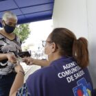 Agente de saúde sentada confere documento de paciente em pé