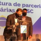 Prefeito Adriano Silva em palco de evento assina documento num púlpito