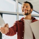 Rapaz jovem está sorrindo e aperta a mão de outra pessoa, cumprimentando quem está a sua frente