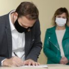 Prefeito Adriano Silva assina documento e é observado pela vice-prefeita Rejane Gambin