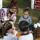 Professora de educação infantil sentada no chão, em roda, com alunos que a observam