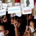 Estudantes, com máscaras, seguram cartazes com as palavras igualdade e somos todos iguais