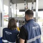 Dois fiscais do Procon anotam dados em frente a uma bomba de gasolina