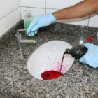 Homem despeja corante em uma pia de banheiro para verificar se a água está escoando para a rede