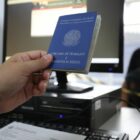 Atendente segura uma carteira de trabalho na frente de um homem que está sentado