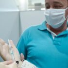 Homem com máscara olha para a mão de uma profissional que segura uma seringa com vacina contra Covid