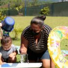 Crianças pequenas brincam com uma professora em um centro de educação infantil. Elas usam baldes, bóias e água.