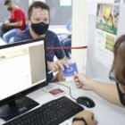Homem entrega carteira de trabalho a um atendente sentado em frente a um computador