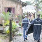 Agentes da Defesa Civil carregam lona em direção a uma casa