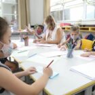 alunos da rede municipal sentados ao redor da mesa e professora auxilia nas atividades