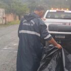 Homem com capa de chuva da Defesa Civil de Joinville carrega uma lona em direção a um carro