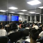 alunos em sala de aula com duas telas digitais a frente