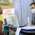 Servidor com máscara atende uma mulher em stand de procura de emprego