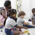 Crianças da educação infantil fazem atividades sentados no chão ao lado de professoras