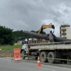 Parte da rua interditada, um caminhão parado com tubulação sendo descarregada por trabalhadores