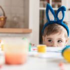 Criança, com tiara de coelhinho, olha para uma mesa com ovinhos