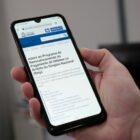 Mão de uma pessoa segurando um celular no site da prefeitura