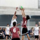 Meninos dividem bola em rede de vôlei durante partida
