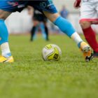Dois jogadores de futebol disputam uma bola em partida em um campo