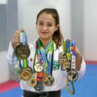 Atleta de karatê com muitas medalhas no pescoço e nas mãos