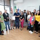 Prefeito e grupo de pessoas posam para foto segurando nova lei sancionada