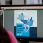 Mulher olha para tela do computador na página do Atlas de Variação em Saúde do Brasil.