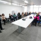 Palestrante, em pé, fala para pessoas sentadas atentas a ele, em uma sala