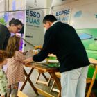 Duas crianças e a mãe recebem orientações de um funcionário da Companhia no stand da empresa na feira do livro