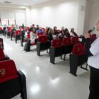 Servidores sentados em cadeiras observam palestrante em pé com microfone