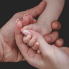mãos de dois adultos seguram a mão de um bebê