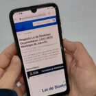 Mão segura um celular no site da prefeitura com informações sobre LDO