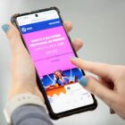 Mão de mulher segura celular na página do PROA
