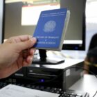 Pessoa segura carteira de trabalho ao atender trabalhador, sentado, de máscara