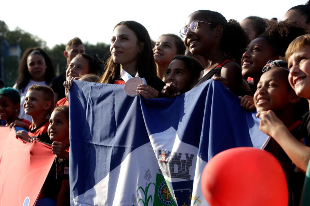 Leticia Oro segura a bandeira de Joinville ao lado dos colegas de equipe