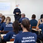 Guardas municipais sentados, em sala de aula, com instrutor a frente