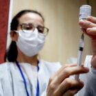 Enfermeira, com máscara e óculos, manipula seringa e frasco com vacina