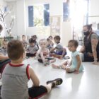 Alunos da educação infantil sentados em sala de aula, em roda, junto com professoras, realizando atividades