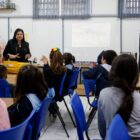 Professora, em sala de aula, apresenta trabalho para alunos sentados