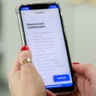 Mão de mulher segura celular na página do Joinville Fácil