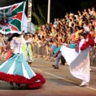 Porta bandeira e mestre salas desfilam na avenida observados por plateia