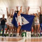 Jogadoras de basquete comemoram em quadra segurando a bandeira de Joinville