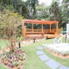 Espaço com deck de madeira, bancos, pergolado e flores