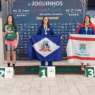 Atleta de Joinville, segura bandeira da cidade, em pódio onde ocupa o primeiro lugar ao lado de outras duas atletas
