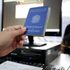Atendente segura carteira de trabalho na frente de computador e trabalhador espera