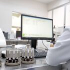 Técnica olha para o computador, ao lado de amostras, em laboratório