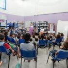 Alunos, sentados em cadeiras, acompanham contação de histórias