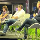 Prefeito de Joinville, em palco, ao lado de outros dois convidados